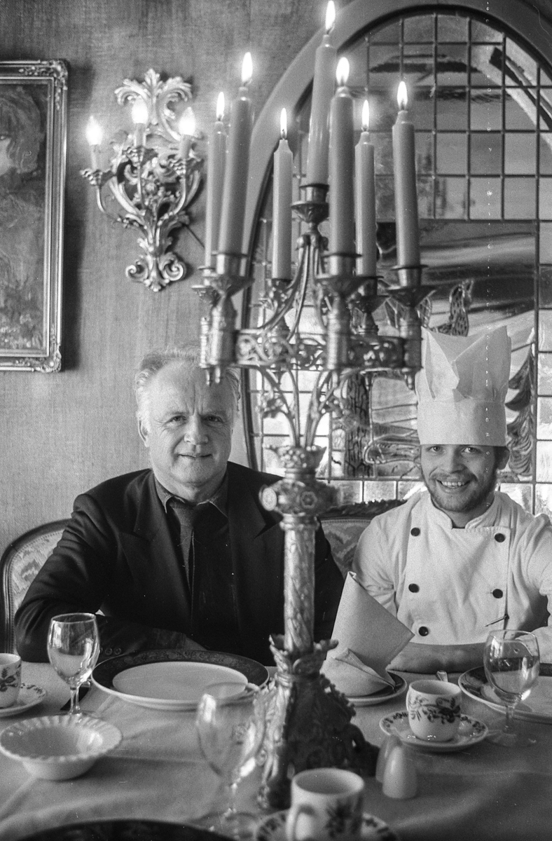 Villa Sandvigen, far John Normann Henriksen og sønn med kokkelue, sitter i restauranten ved et pent dekket bord.