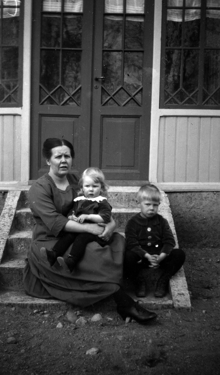 En kvinna och två barn sitter på en trappa vid en ytterdörr.