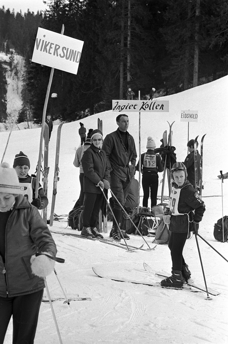 Ungdom med ski samlet rundt mange plakater med forskjellige idrettslag, "Aprilspøken" slalåmrenn i Tryvannskleiva. Fotografert 23. mars 1969.