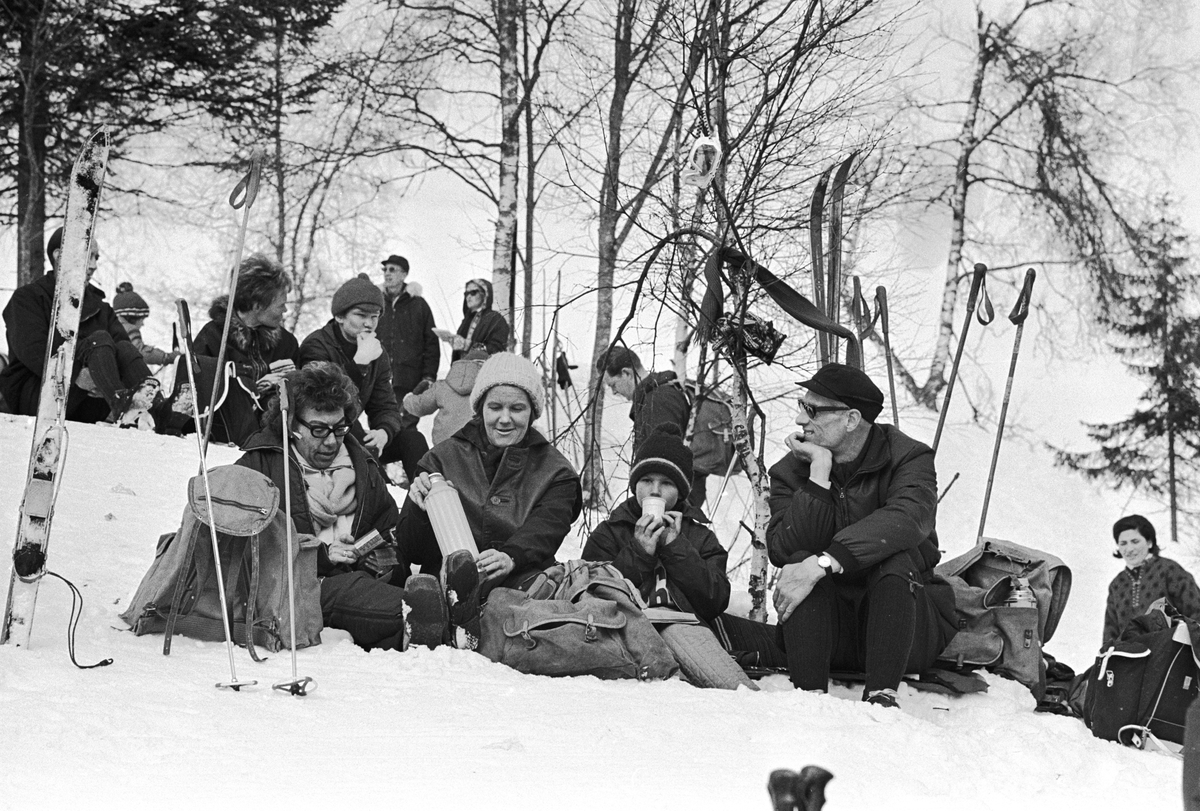 Tilskuere sitter langs løypa, "Aprilspøken" slalåmrenn i Tryvannskleiva. Fotografert 23. mars 1969.