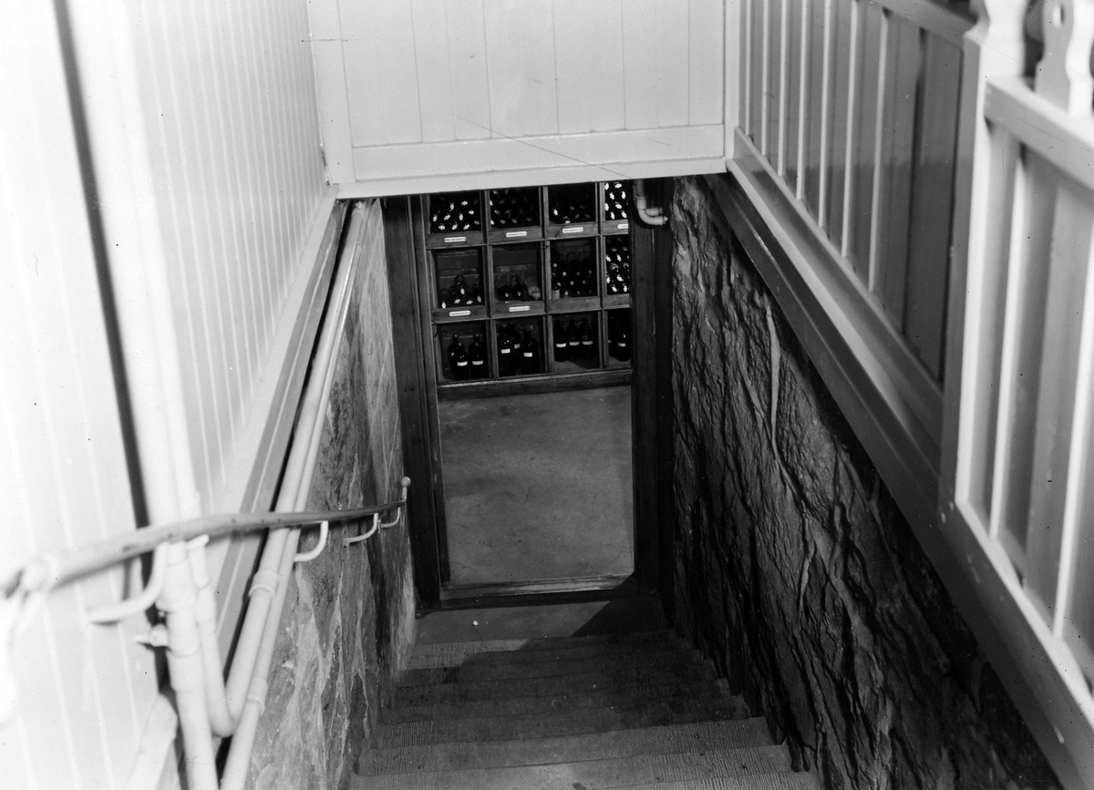 Nedgången till vattenkällaren på apoteket Hjorten. Bilden visar en trappnedgång, i dörröppningen syns hyllor med flaskor på.