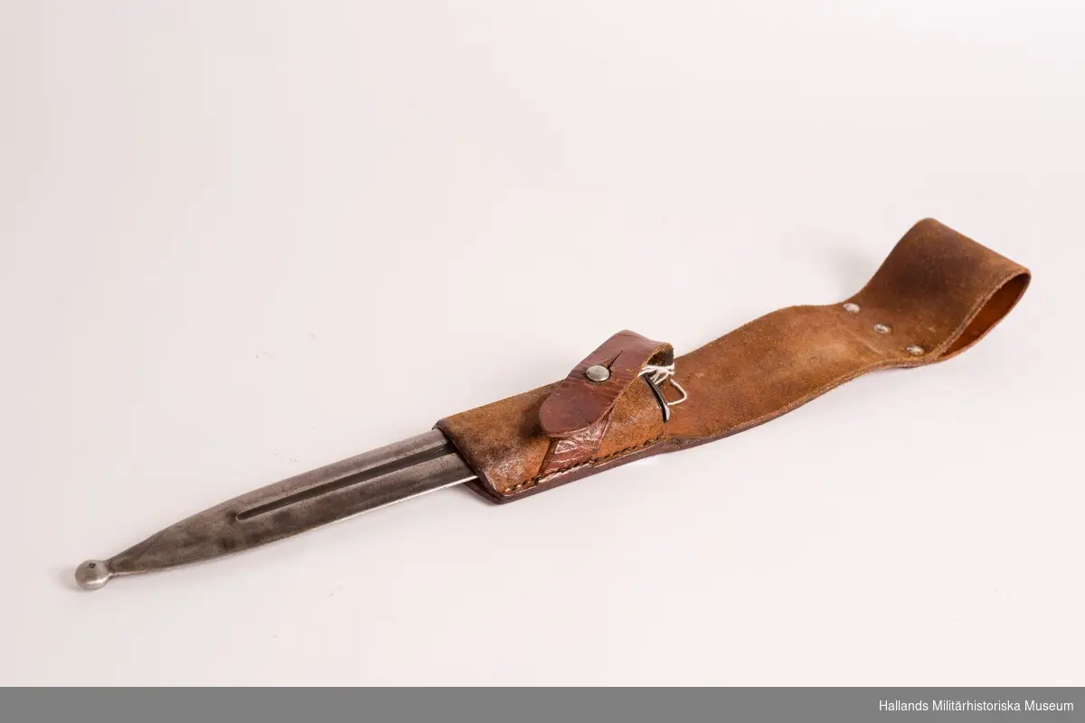 Bajonetthylsa för knivbajonett m/1896. Tillverkad i brunt läder. Baljan fästes i hylsan med hjälp av läderrem och mässingsknopp.