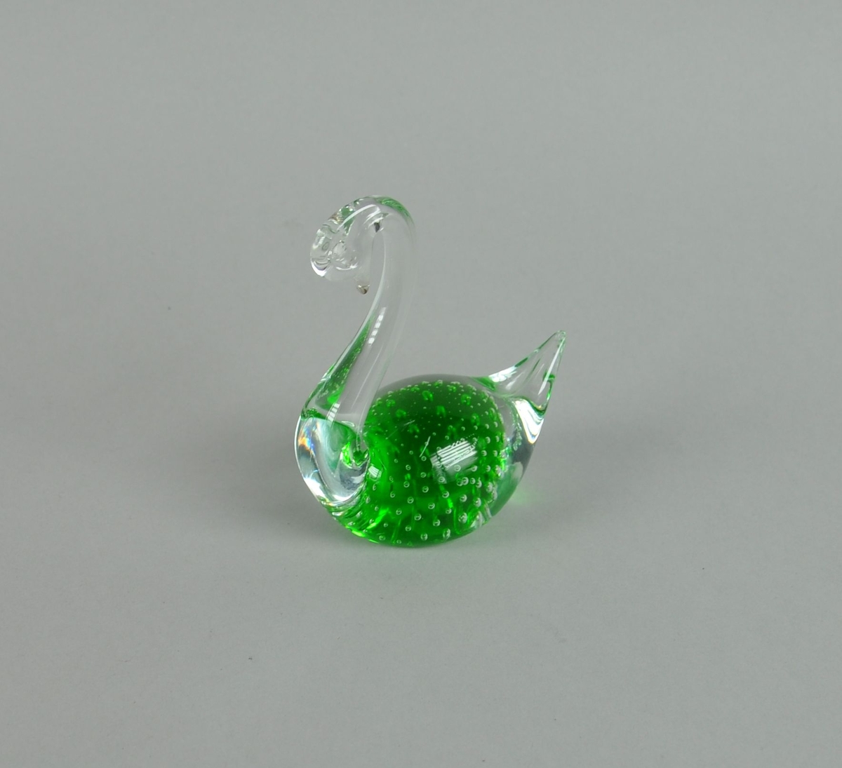 Glassfigur, forestiller svane. Glasset er grønt i midten, med dekorative bobler.