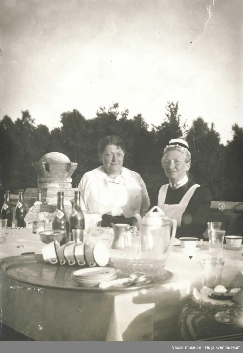 Anna Marensson med hushjelp sitter ved halvveis dekket bord, 1931.