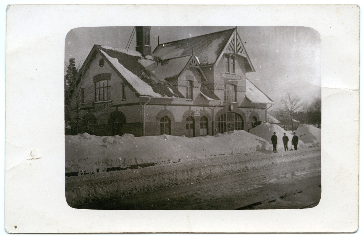 Personal med spadar snöröjer framför stationshuset.