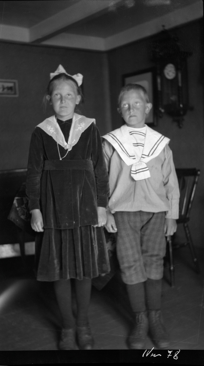 Portrett av pike og gutt stående i stue.