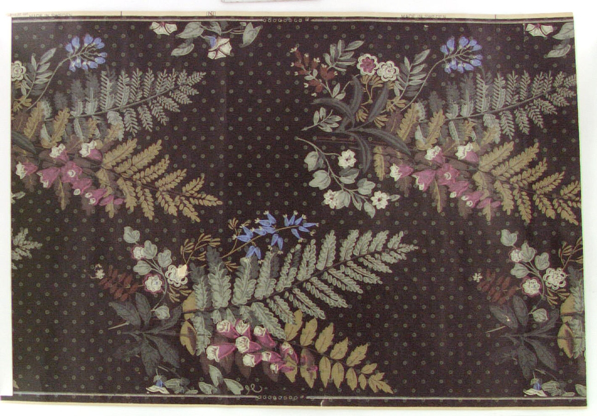 Tapet med buketter av vilda blommor i ceriserosa, grönt, blått och beige. Tryckt s.k. patentbotten i svart med gröna prickar. Tillverkad av Norrköpings Tapetfabrik. VE