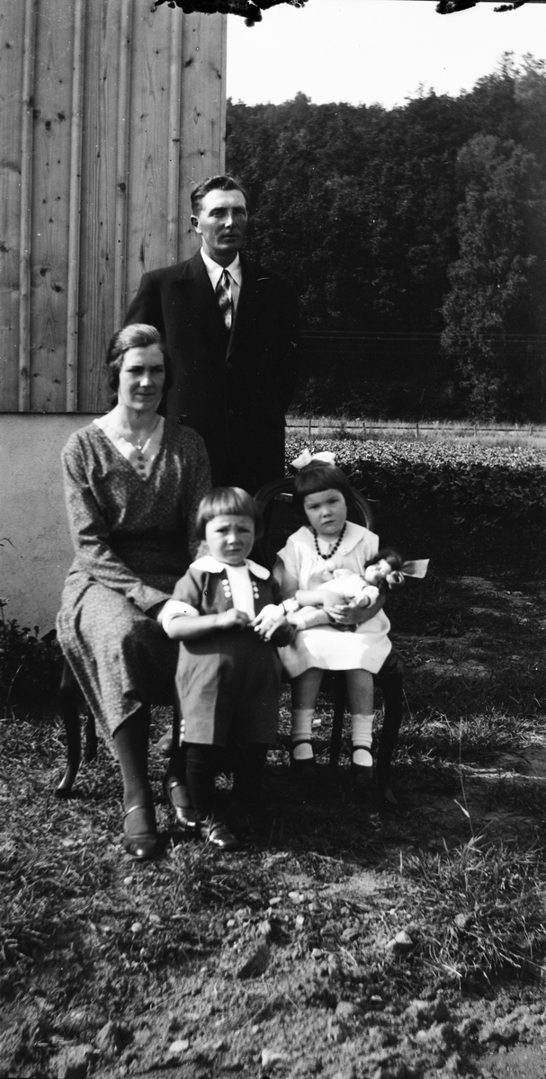 Familjen Henriksson på Lövagård fotograferade vid husknuten. Dottern Maj-Britt sitter och håller i en docka, båda med rosett i håret, och sonen Ingvar (eller möjligen dottern Kerstin) står i kolt, långstrumpor och blanka skor.