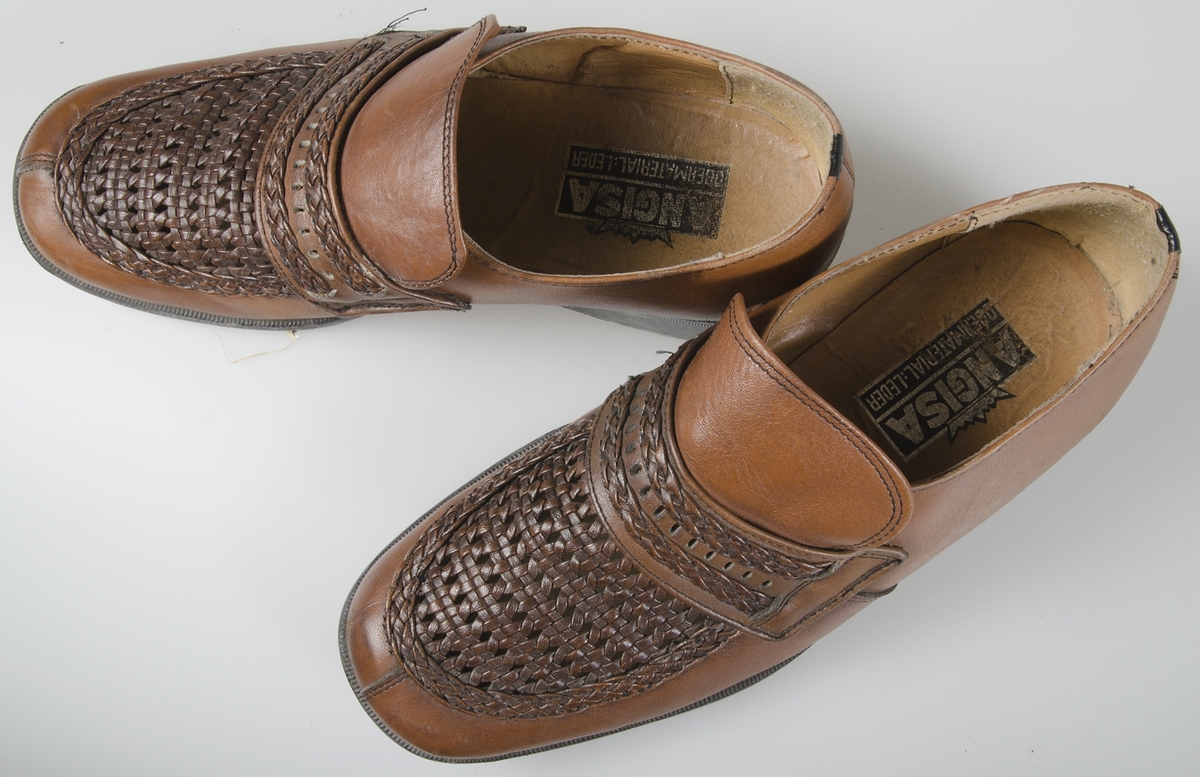 Ett par skor (loafers) av ljusbrunt läder med flätad överdel. Gummisulor. Maskinsydda. Söm vid tårna. Storlek 42. Lite räfflade klackar. Märkt: ANGLISA, OBERMATERIAL-LEDER.Samhörande med nr. UM 19115-19188.