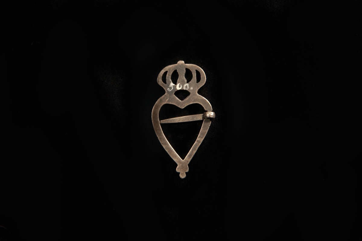 Ett hjärtformat spänne av silver med genombruten krona överst.
