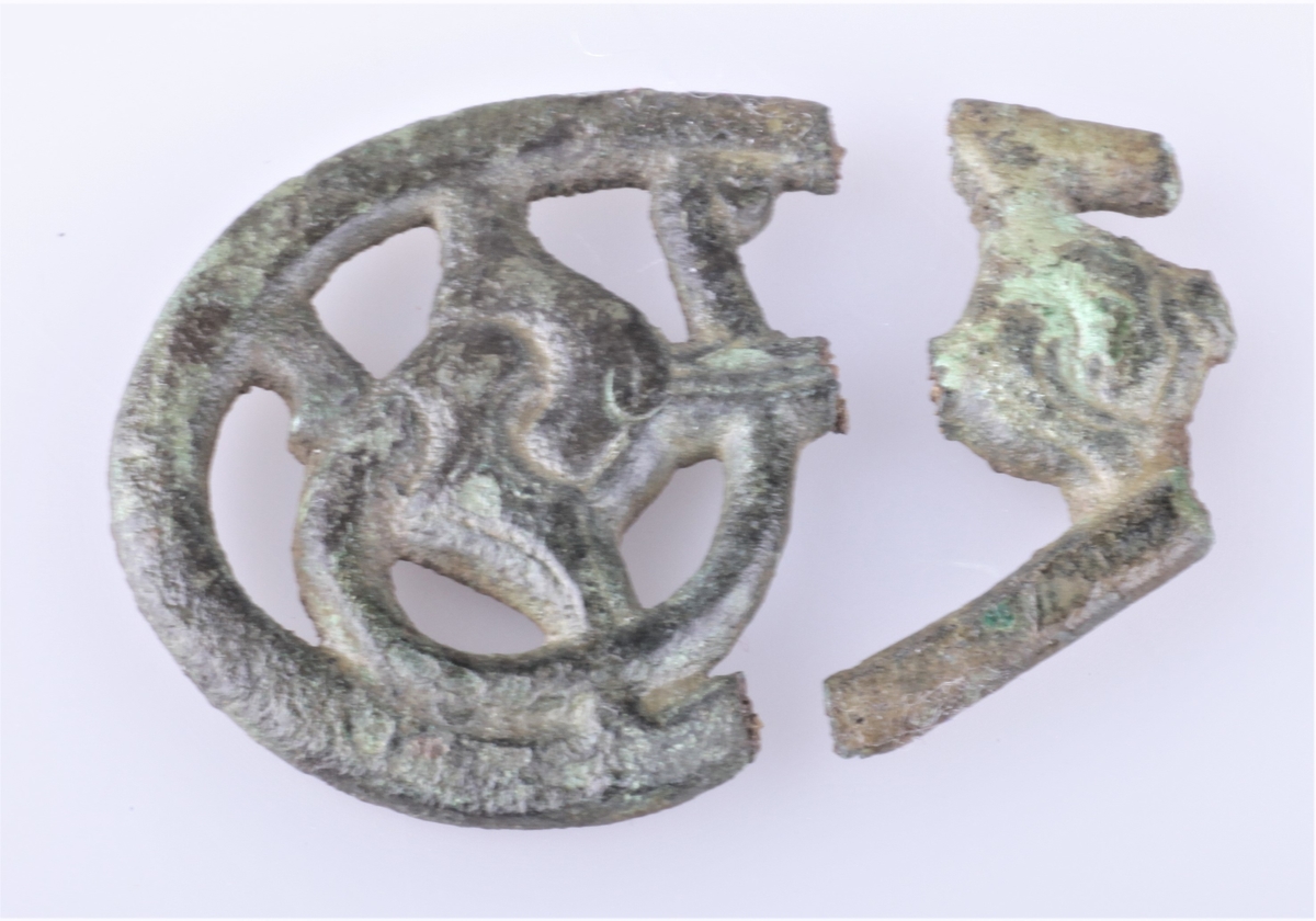 Nøkkelskaft støpt i bronse med gripedyrsmotiv. To deler; a) hoveddelen har avlang buet form, b) del falt av hoveddelen.