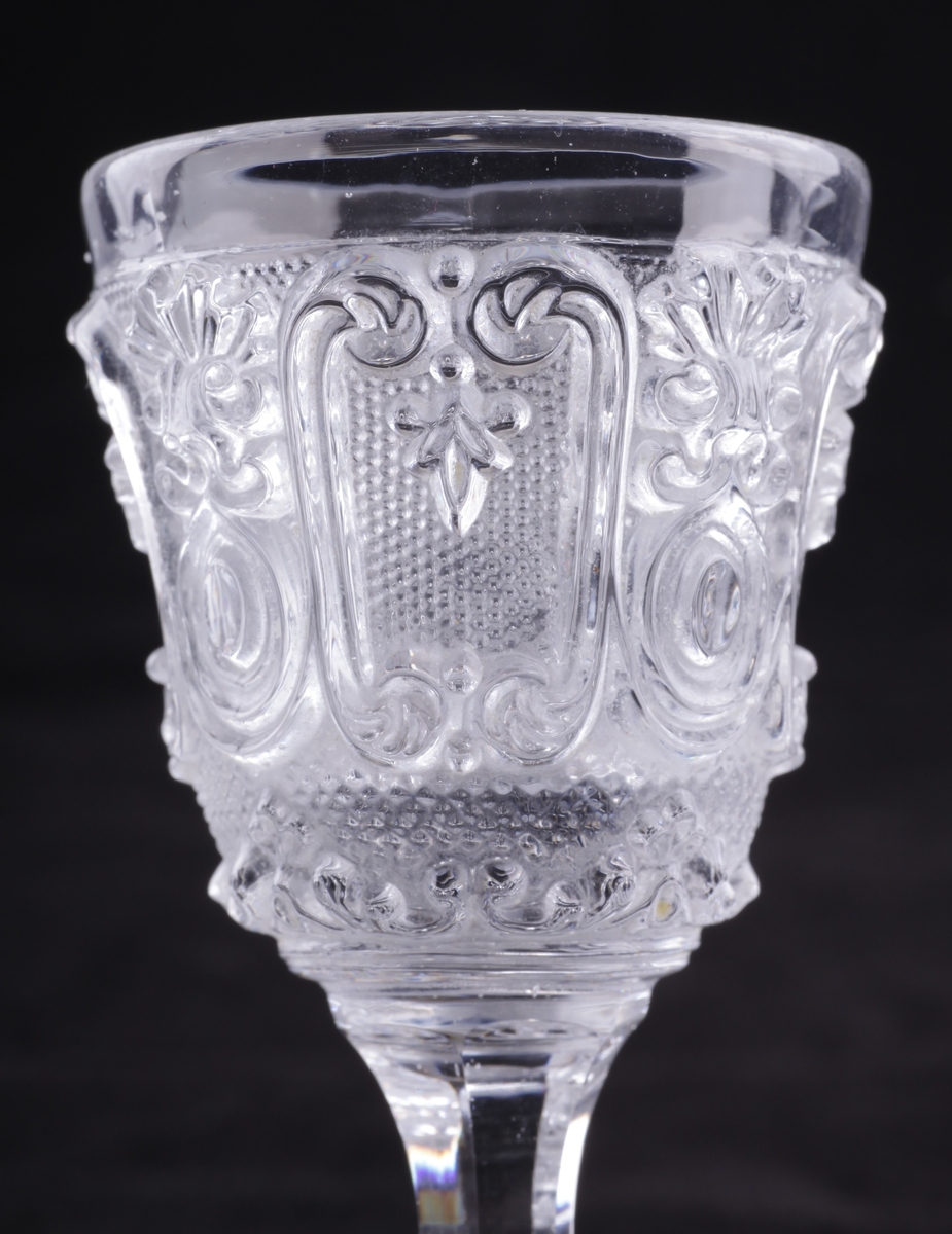 Drammeglass i pressglass, med slipt stett og fotplate. Samme mønster som karaffelen nr EKM-10257.