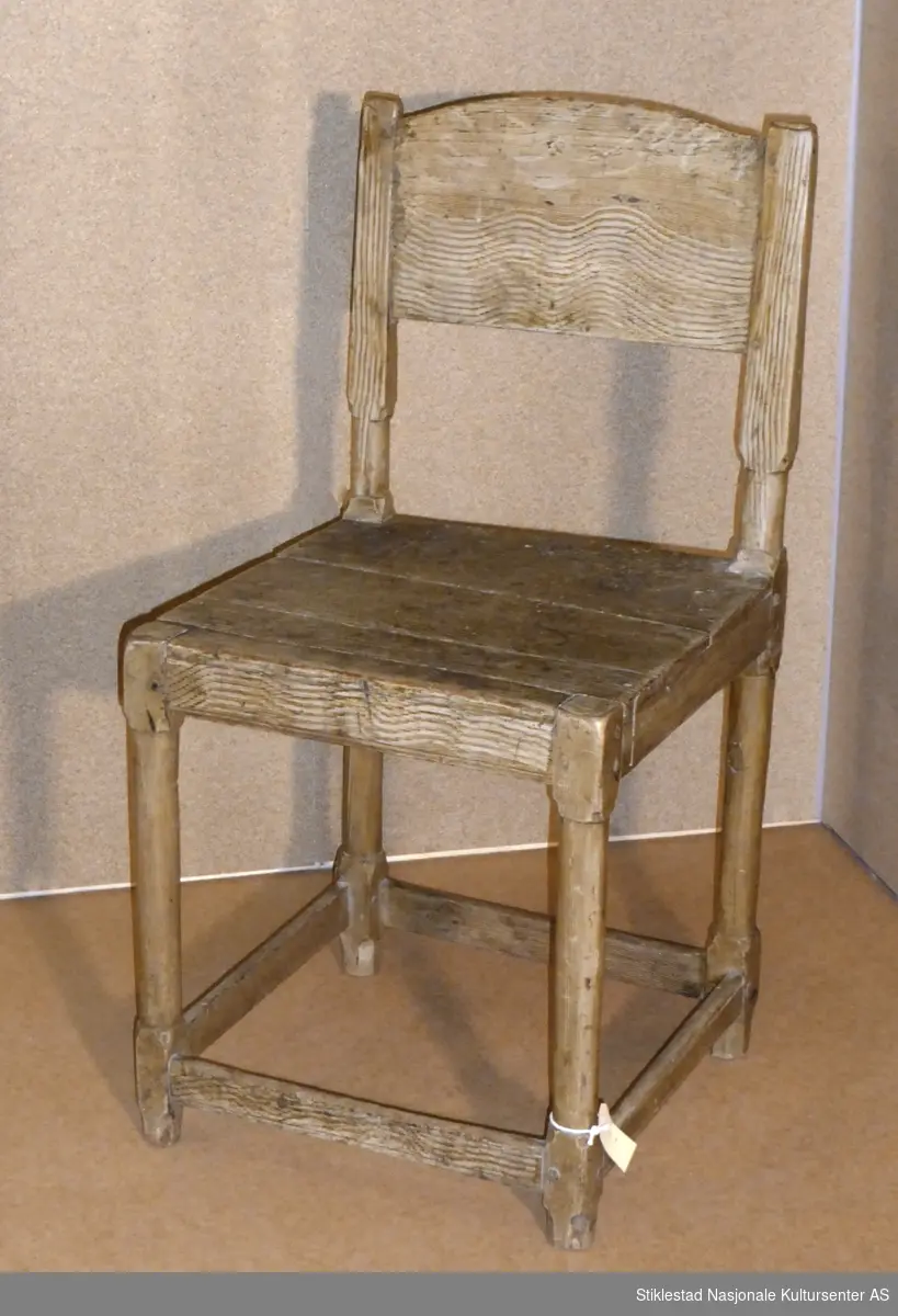 Stol i renesanselignende stil, ca. 1700. Sete laget av to bord, sprukket. Dreide (eller spikket/teljet) føtter som er tappet inn og naglet til sidesarg/ramme. Ryggbrett er et bord med buet topp. Grovt åringsmalt. Lavt sprossverk (avstivere). Merket med krittmerke under sete.