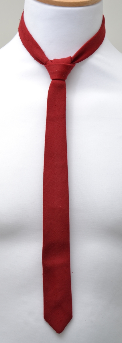 Korpsuniform bestående av jakke, skjorte, slips,to skjørt, hansker og lue. Jakken er dobbeltspent med 4 metallknapper, skulderklaffer og et felt med et smalt hvitt bånd på armene. Skjørtene er grå og plisserte og lukkes med knapp og trykknapper. Enkel hvit skjorte med rødt slips til. Uniformsluen er rød med hvite bånd og dusk i pannen. Et par hvite bomullshansker hører til. Jakken er i størrelse 10 år.