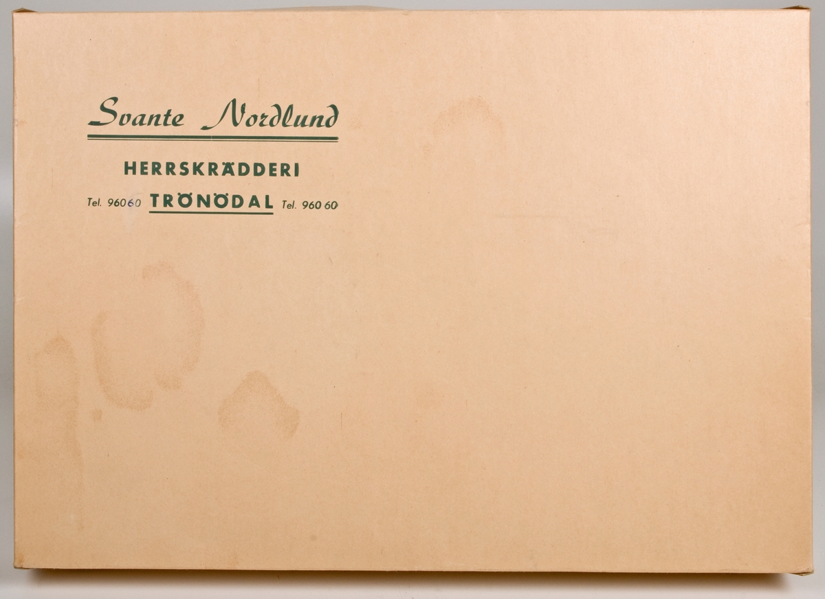 Skräddarkartong i gulvit papp med grönt tryck: "Svante Nordlund HERRSKRÄDDERI TRÖNÖDAL Tel. 960 60".