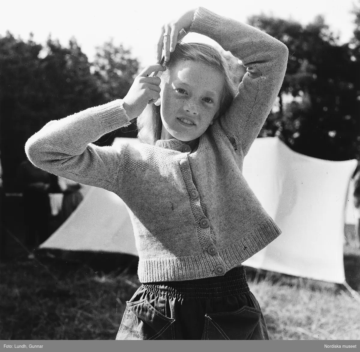 En flicka kammar håret på Mölle camping år 1952. Ett tält i bakgrunden.
