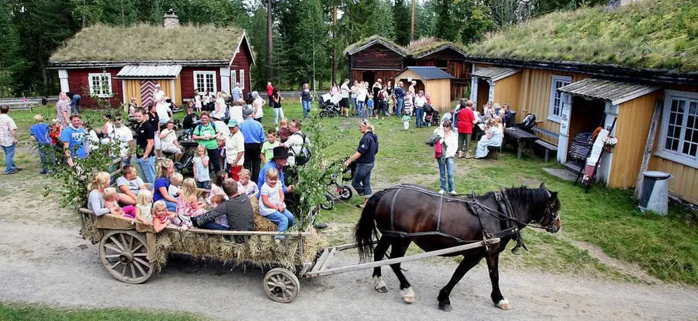 Bildet viser Elverumstunet på Glomdalsmuseet under et arrangemen. I forgrunnen ser man mange barn som sitter i en vogn dratt av en hest.