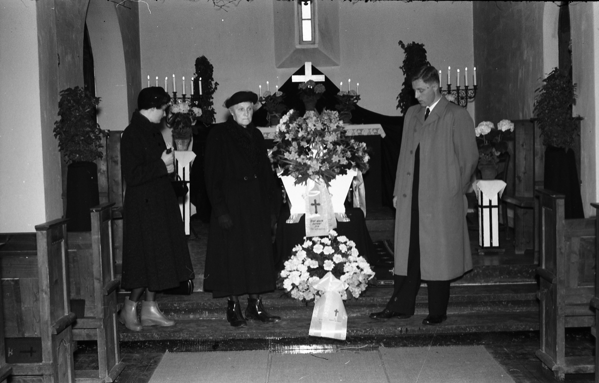 Tre bilder fra en begravelse. Bildene er tatt inne i kirke eller gravkapell, ukjent hvor. På det første bildet er tre uidentifiserte personer samlet ved kista. De to øvrige viser kiste og kranser.