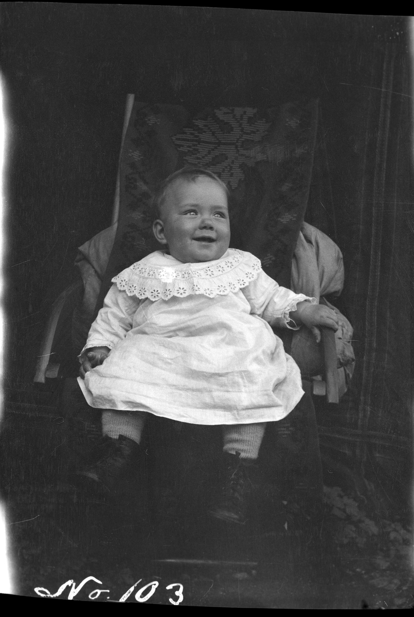 Portrett av et lite barn sittende i stol.