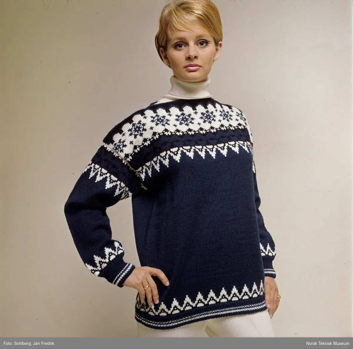 Kvinnelig modell viser høst/vintermote; en blå strikkegenser med hvitt mønster.