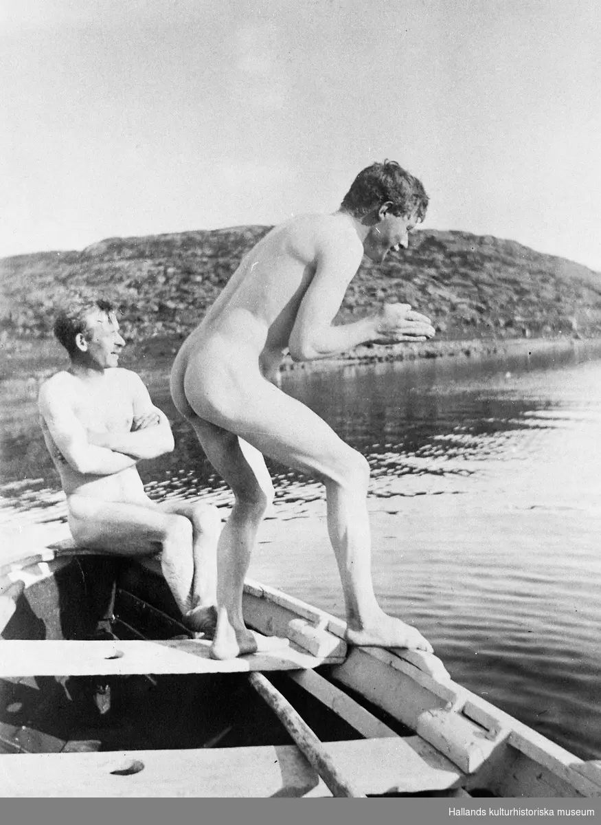 Två nakna män i en båt vid Onsalahalvön. Knut Larsson sitter i fören och hans bror Torsten står på relingen i dykposition. I bakgrunden kala berg.