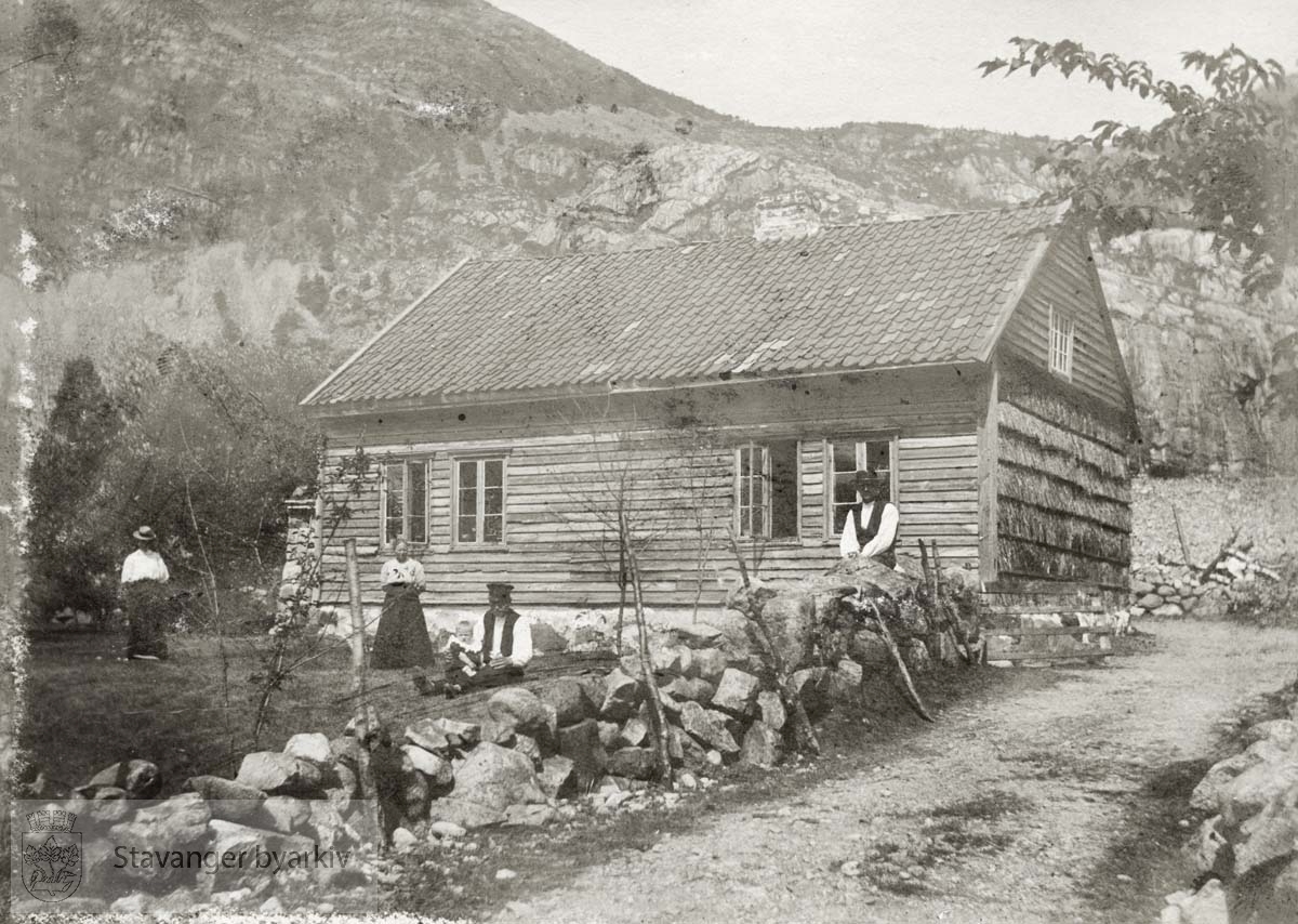 To menn og to kvinner foran hus i fjellet.