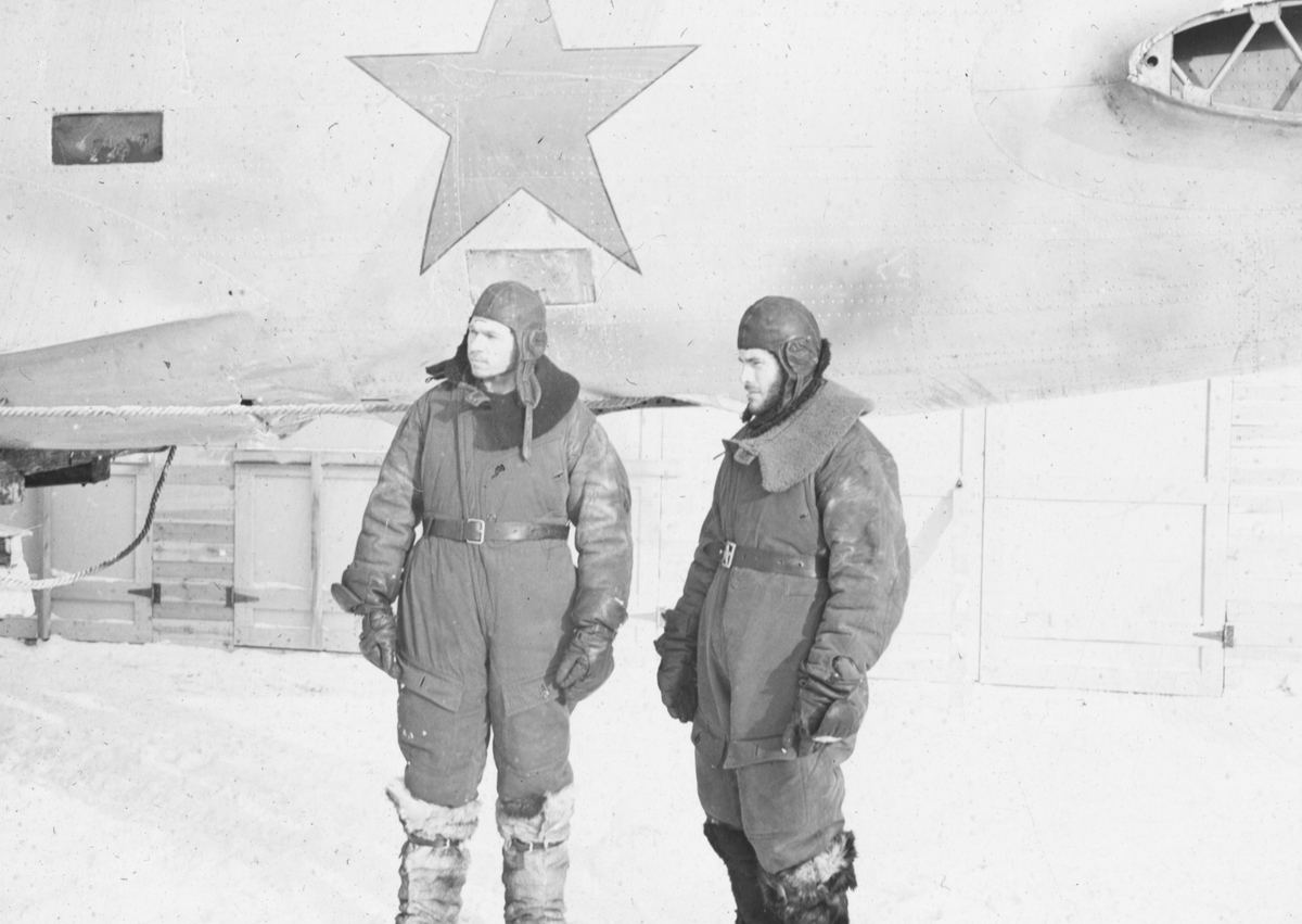 Sovjetiska flygare som tagits som krigsfångar. I bakgrunden det nedskjutna sovjetiskta flygplanet DB-3 lastat på vagn vid Svenska frivilligkåren i Finland, F 19.