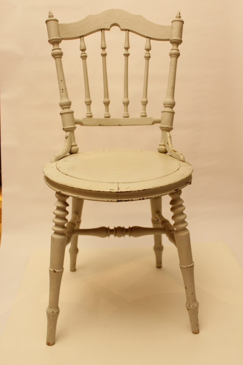 Nyrenässansstol som senare är målad i ljust grått. Dekoren syns genom färgen. Ryggstycke med svarvade pinnar. Rund stolsits, svarvade ben, svarvat benkryss.