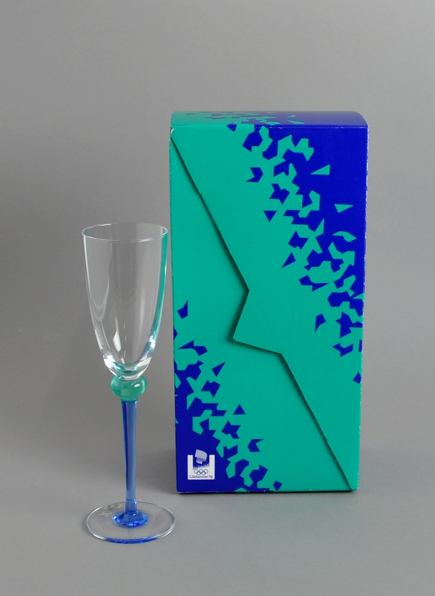 Hvitvinsglass med blått stett med fakkelmann, turkis kant like under glasset. Glasset ligger i original emballasje.