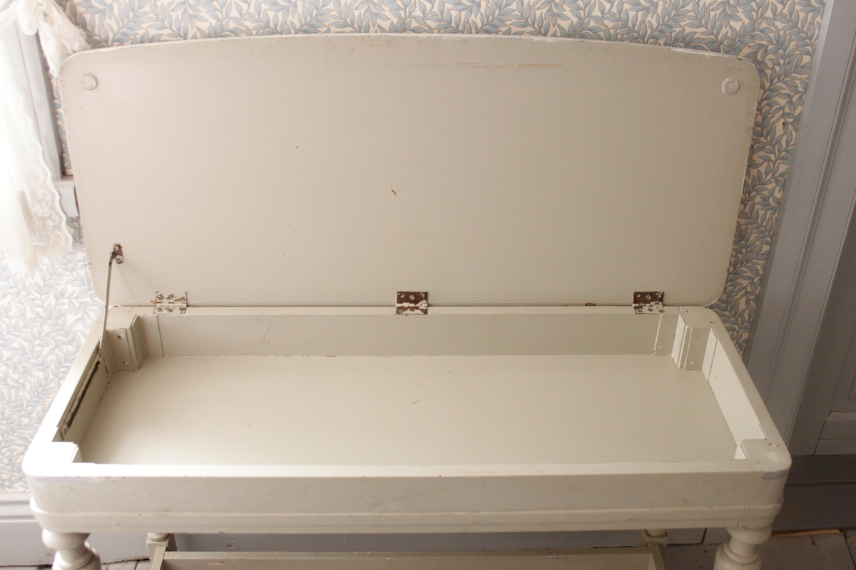 Lågt gråmålat bord med svarvade ben och tre tvärslåar mellan benen. Med en uppfällbar bordsskiva som döljer en låda i bordets sarg.