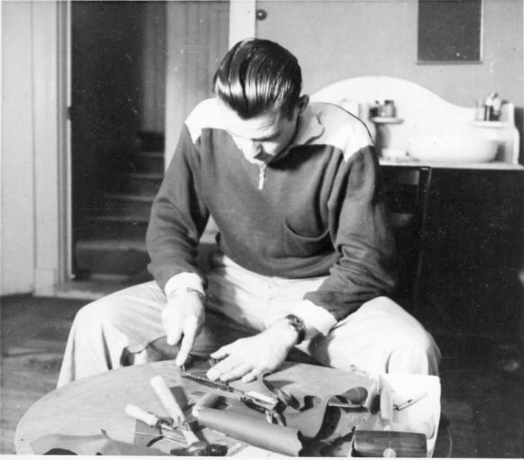 En man sitter lutad över ett bord och skär bitar i läder efter en mall.