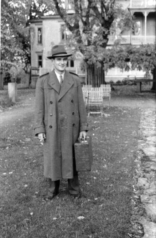En man i rock och hatt i Ribbagården trädgård. Cigarett i ena handen och en resväska i den andra.