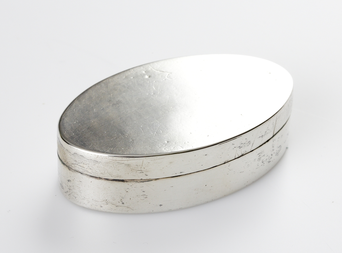 Dosa, silver.
Oval, slät modell. Invändigt förgylld. Ägarinitialer: "J.O.D." på dosans undersida. 
Stämplar (något otydliga) på lockets undersida.