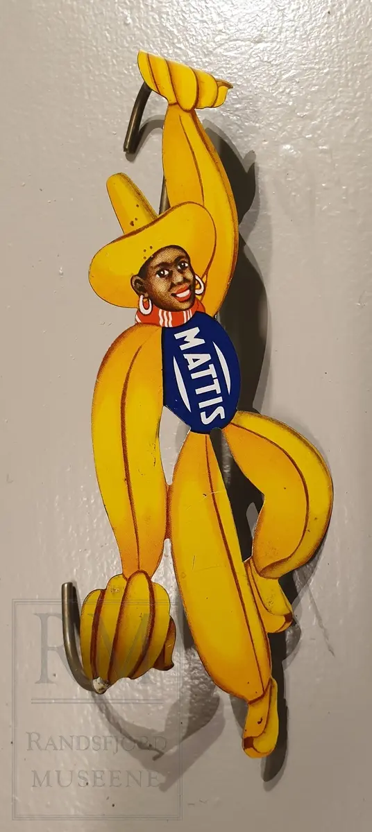 Mørkhudet mannsperson med banandrakt og hatt, holder en bananklase i hver hånd