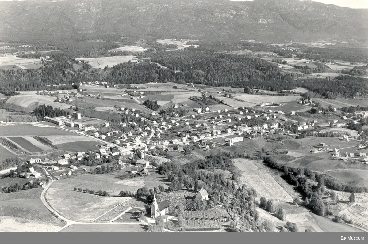 Flyfoto av Bøhaugen med kyrkjene og Midt-Bø gardane, tatt 5. juli 1952.