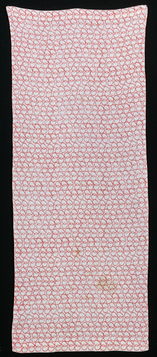 En gardinvåd av bomull med handtryckt mönster, rött mot vit botten. Kallas "Kringlan" eftersom mönstret är i form av kringlor. Vävt av Jobs i Leksand för Gefle Ångväveris räkning i slutet av 1940-talet eller början på 1950-talet. Några fläckar.