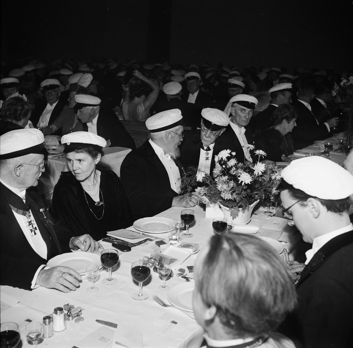 Män och kvinnor i studentmössor vid dukat festbord på rikssalsbanketten i samband med Östgöta nations 300-årsjubileum, Uppsala 1946