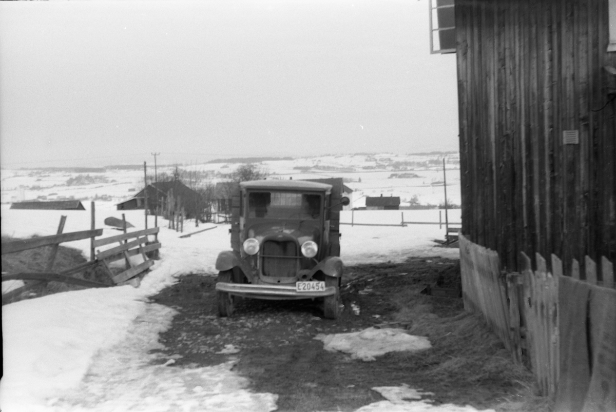 Snødekt landskap med en liten lastebil i forgrunnen. Litt lengre bak bygninger på gården Skjefstad i Lensbygda. Fotrografens standplass har trolig vært ved Sveiserbygningen på Nordre Rise. Bilen skal iflg. informant være en Ford pickup av årsmodell 1928-29..