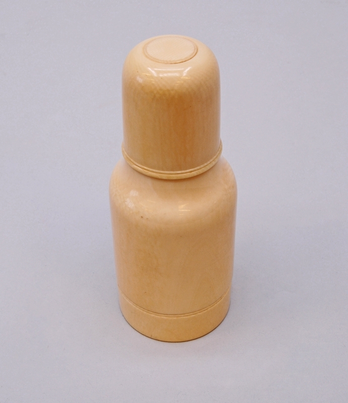 Gräddvit flaska (A) av elfenben, med kork (B) och botten(C) som går att skruva loss. I denna finns ytterligare en flaska (D) av kristallglas, med propp (E). 

Den yttre flaskan är formad som en cylinder som smalnar av upp mot korken. Botten på flaskan är klädd i filt. 
Den inre glasflaskan är formad som den yttre, och har ett kvadratiskt rutmönster i relief. Proppen är halvklotformad och har samma dekorationer som flaskan på sidorna, samt ett blommönster i relief ovanpå.