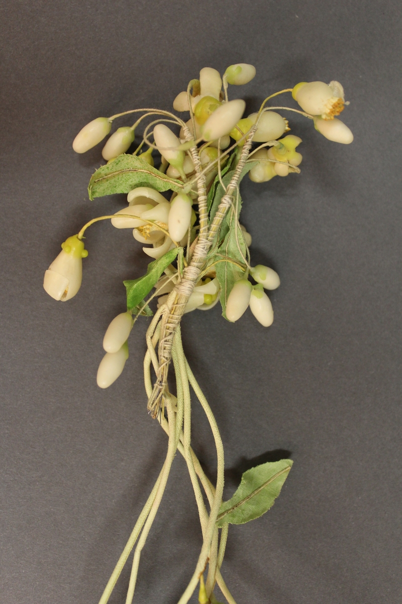 Applikation till brudklänning. Blomsterutsmyckning av vitt vax på grönt papper.