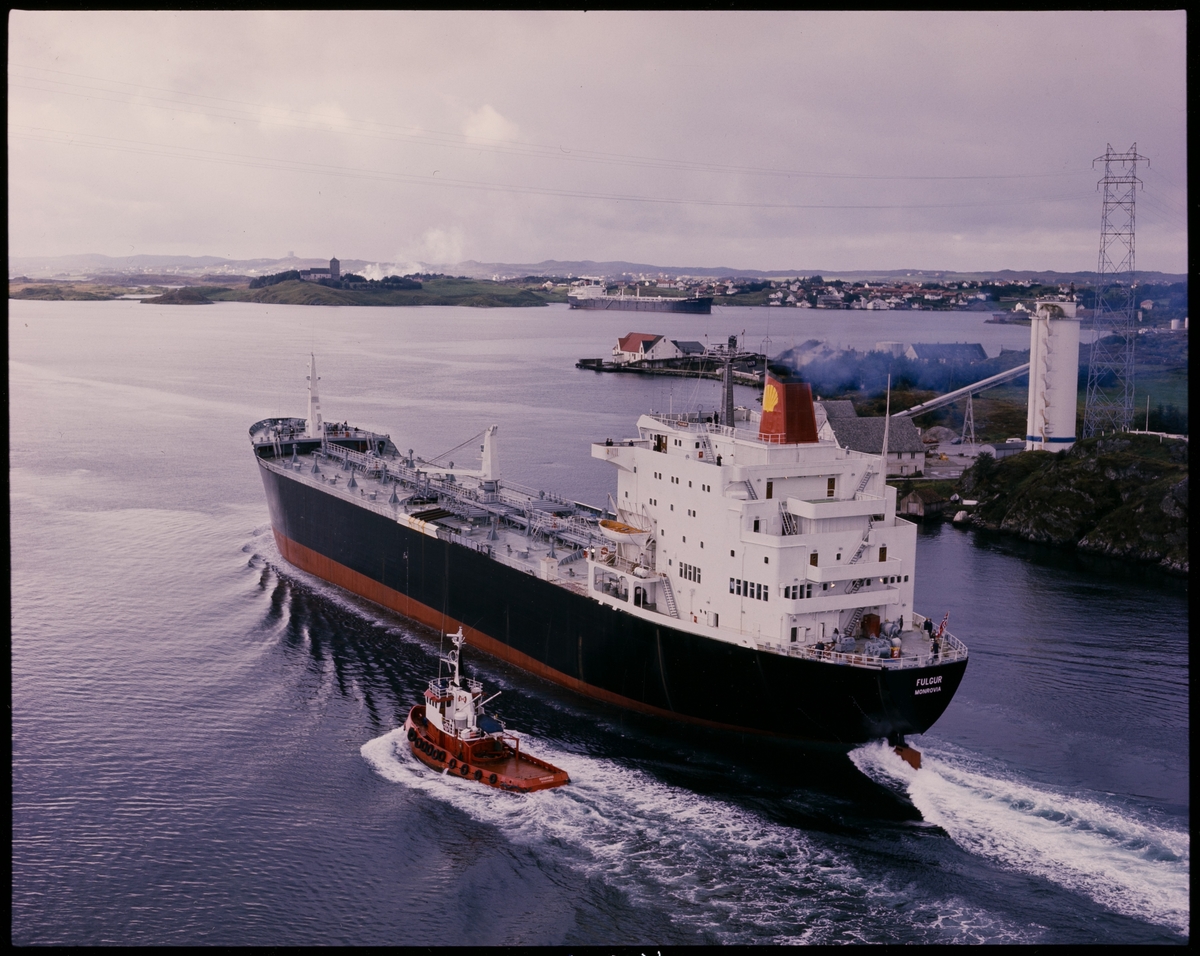 Tankskipet "M/S Fulgur" fra Monrovia passerer Karmsundbrua i retning sørover. Skipet er bygget for Shell. Taubåten "Haabrand" fra Stavanger kjører ved siden. "John Knudsen" ligger i Bøvågen.