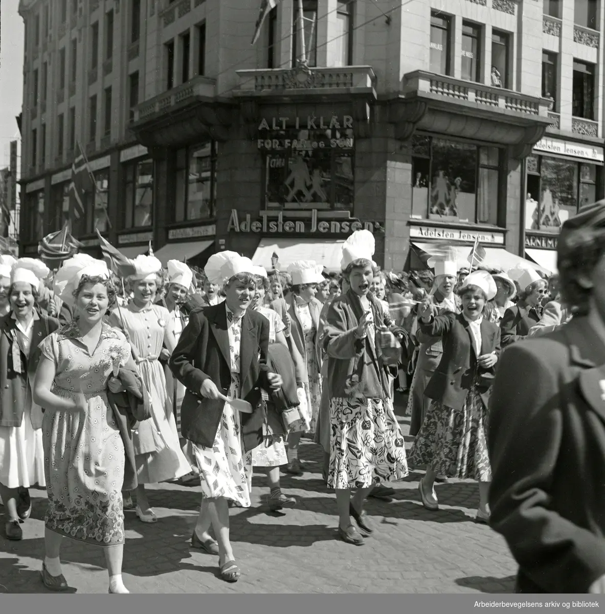17. mai 1952. Unge kvinner med kokkeluer i Barnetoget/Ungdomstoget. Torggata/Stortorget. Hassel-gården i bakgrunnen.