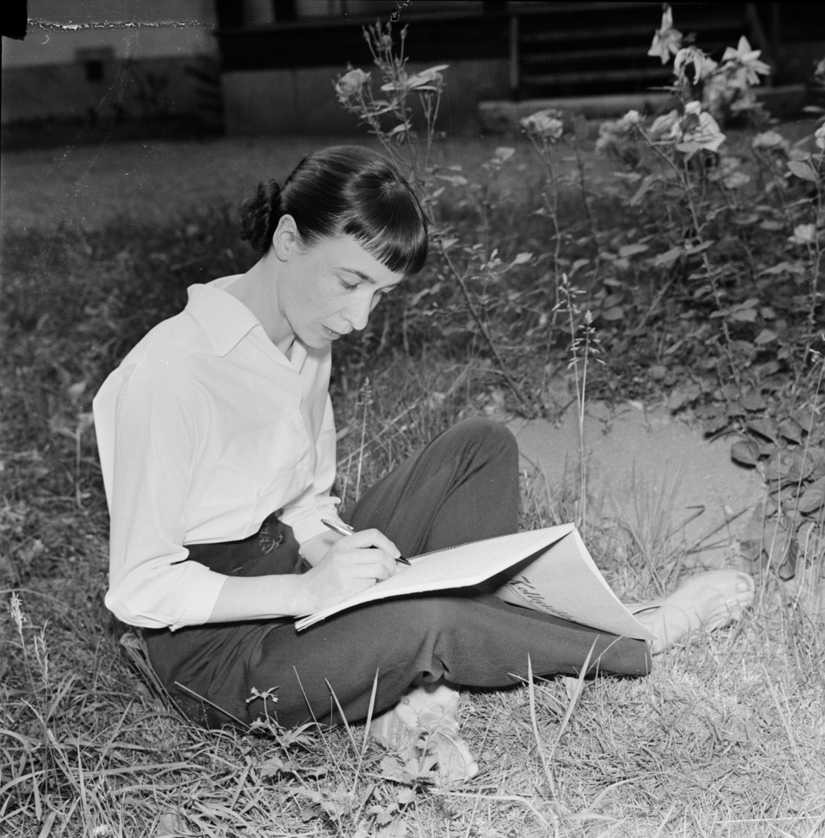 Författarinnan Sara Lidman sitter ute i gräset och skriver, Uppsala 1955