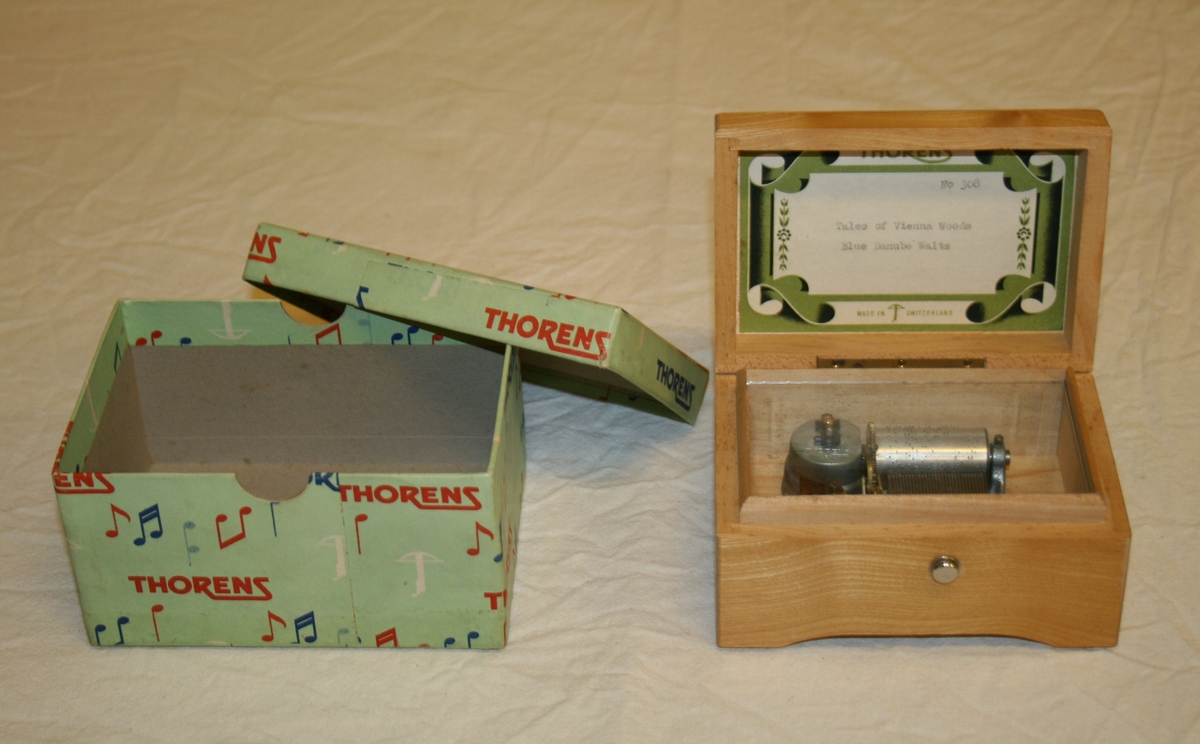 Spilledåse (A) og pappeske (B). Spilledåse i treeske med bilde på lokk. Pappeske med avtagbart lokk. Grønn bakgrunn, pyntet med noter og påskrevet Thorens.
