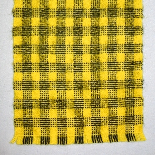 Rutig halsduk vävd i tuskaft med färgeffekt av filtgarn. Varpen och inslaget har samma randning i svart och gult. Det bildas tre olika rutor: en helt gul, en gul med svarta prickar och en randig. På ena sidan är rutan randig på längden och på andra sidan är den randig på tvären. Fransen är 18 och 25 mm lång.

En pappersetikett med LAND textat är fasthäftade i kanten.

Halsduken med modellnamn Citro är formgiven av Ann-Mari Nilsson och tillverkad av Länshemslöjden Skaraborg. Halsduken finns med på sidan 92-93 i vävboken Väv tyger till kläder av Ann-Mari Nilsson i samarbete med Länshemslöjden Skaraborg från 1989, ICA Bokförlag. Se även inv.nr 0041-0096 ur samma bok.