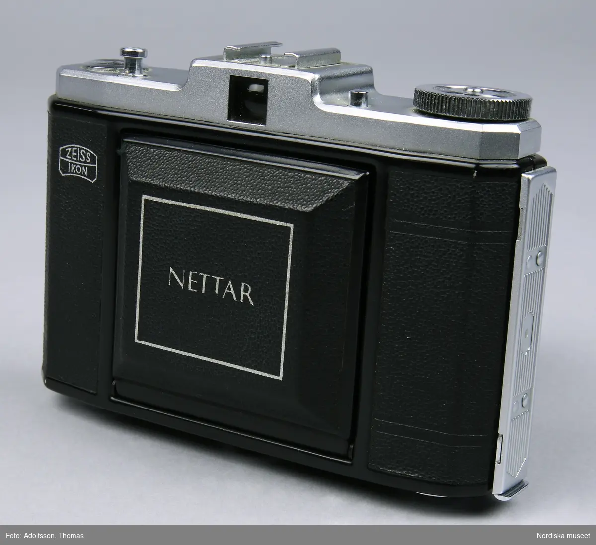 Svart bälgkamera för 60 mm bred rullfilm av märket Zeiss Ikon. Modell Nettar 518/16. Kameran har ett svart hölje av plast. Ovandel i lättmetall.  
Johanna Skoglund 2013-04-02