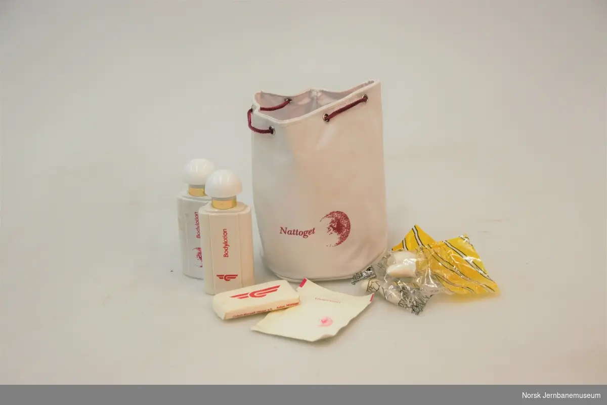 Storage bag from the National State Railways (NSB) night train containing two bottles of body lotion, one bar of soap, two sets of earplugs and a pack of wet wipes. 