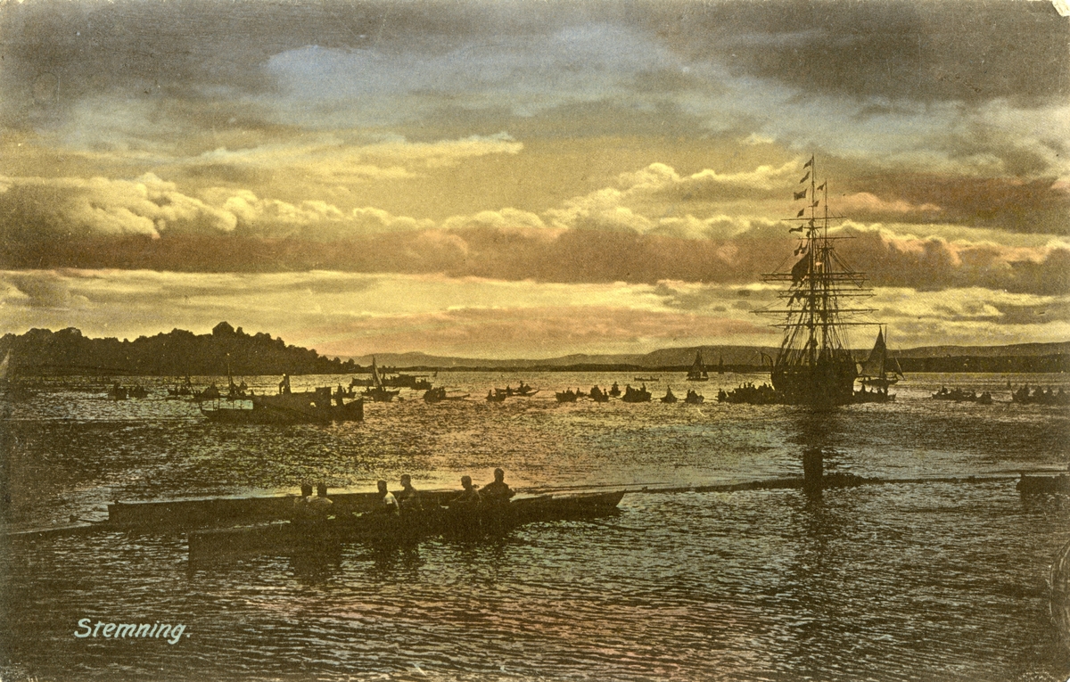 Motiv av en større forsamling båter på sjøen ved solnedgang i Borgundfjorden ved Gåsholmen. I forgrunnen er det seks personer på et ukjent fartøy. Lenger bak ses ei større seilskute omringet av mindre båter.