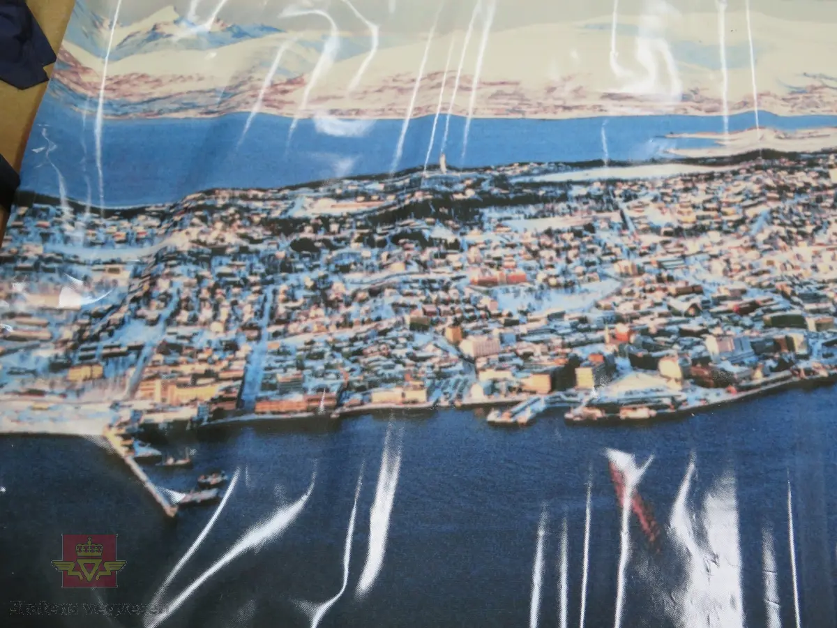 Plakat av plastlignende materiale. Flerfarget. Motivet viser Tromsø by. Plakaten har tekst som informerer om PIARC konferansen i 1990.