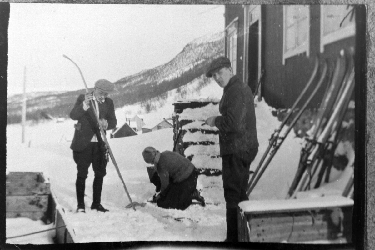 To menn og en kvinne på en gårdsplass klargjør ski før skitur.